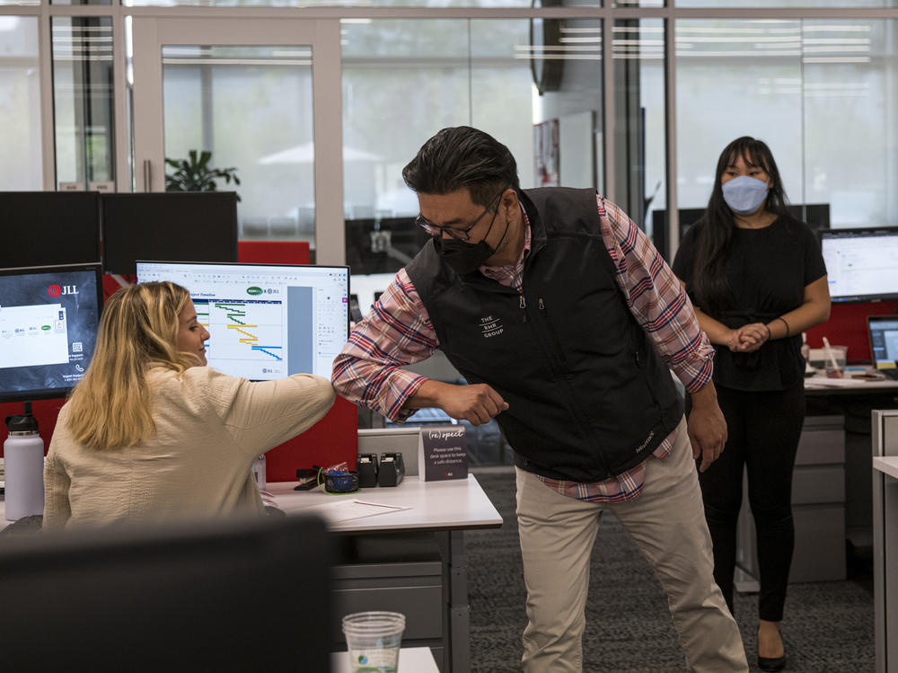 Employees elbow bump at a JLL office in Menlo Park, Calif., in September. With the delta variant surging, mask mandates are returning, and some employers are now requiring employees to be vaccinated before coming to the office.