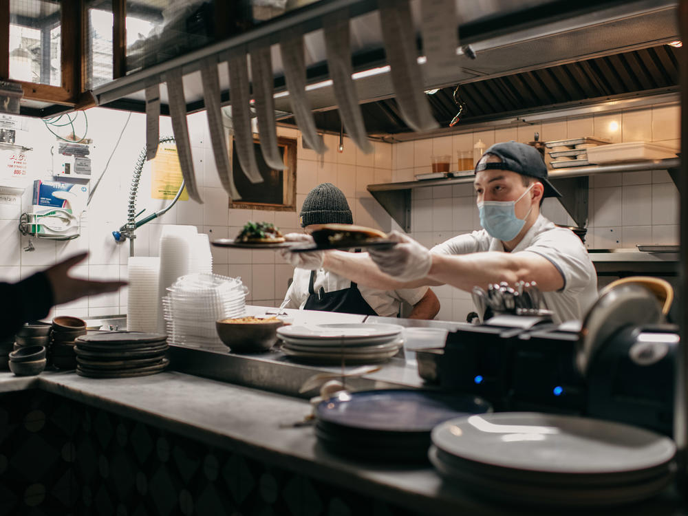 Masked kitchen workers pass plates of food to a server at Claro restaurant in February in New York City. Starting next month, those plates will go only to indoor diners who can prove they have been vaccinated.