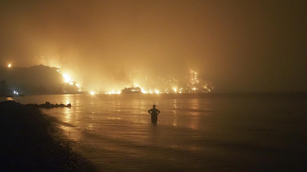 A man watches the flames as wildfire approaches Kochyli beach near Limni village on the island of Evia, about 100 miles north of Athens, Greece, late Friday. Wildfires raged uncontrolled through Greece and Turkey for yet another day Friday, forcing thousands to flee by land and sea.