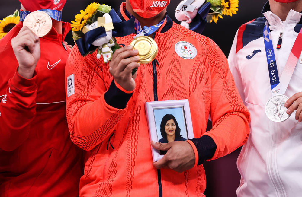 Japan's Ryo Kiyuna holds a portrait of his late mother with his men's kata gold medal at a ceremony in the karate competition.