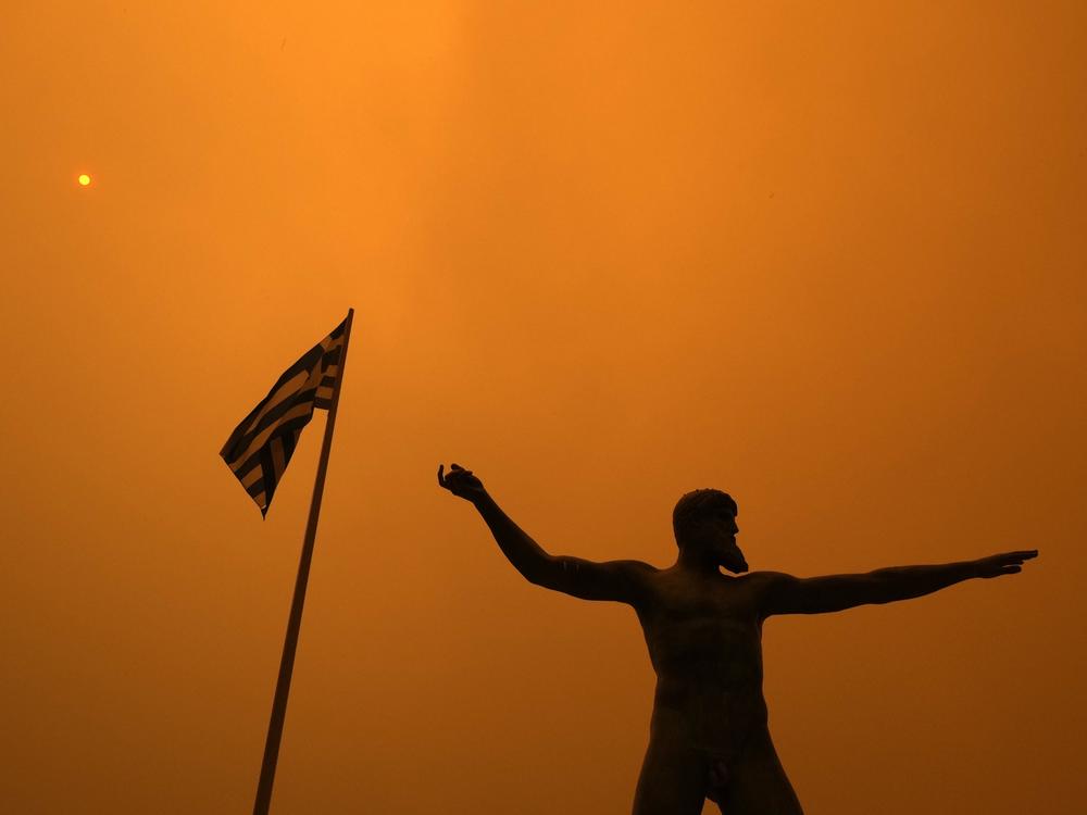 Smoke from wildfire spreads Sunday over the statue of Poseidon, ancient Greek God of the sea, at Pefki village on Evia island, about 118 miles north of Athens.
