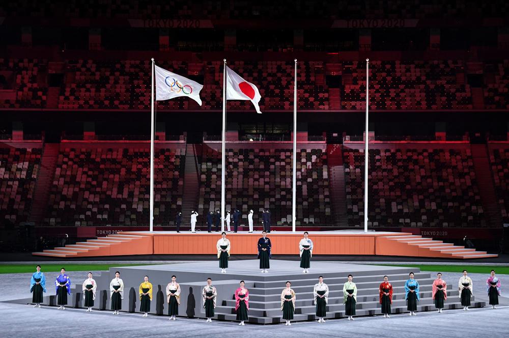 Performers sing the Japanese national anthem as the Olympic flag and Japan's flag are raised.