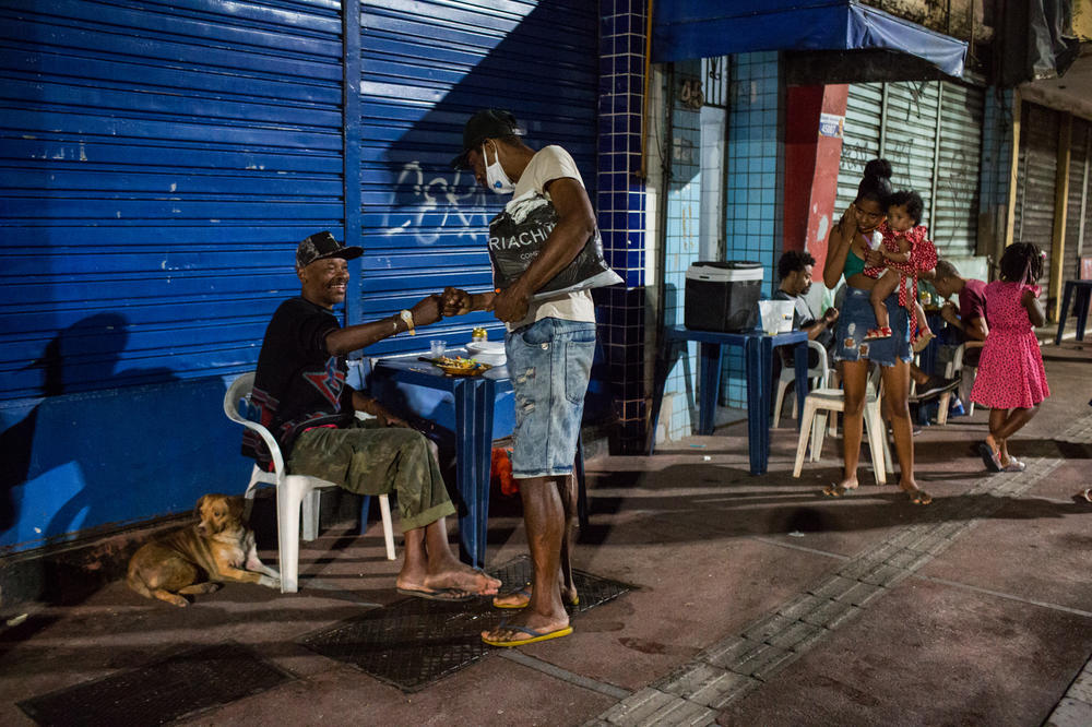 Costa, left, talks to a passerby while eating his meal. Since his wife died a few months ago, he has been living on the streets. Without her income, he can no longer afford their apartment.
