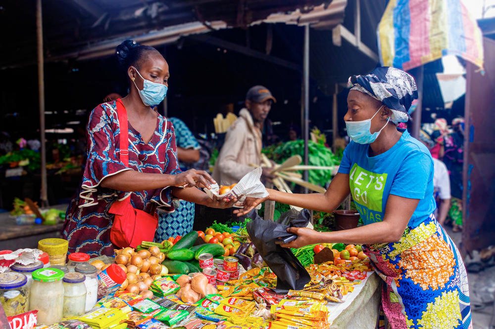Kiali Onzhe Ngssakhes, right, buys vegetables and spices at Talangai Market in Brazzaville, Republic of Congo. The 45-year-old single mother, who is HIV positive, had to stop selling grilled meat due to the pandemic — and now can't buy as much food as she used to.