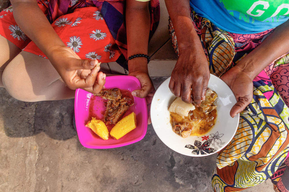 Ngssakhes, right, and her 12-year-old daughter, left, eat boiled plantains and fried fish outside their home.