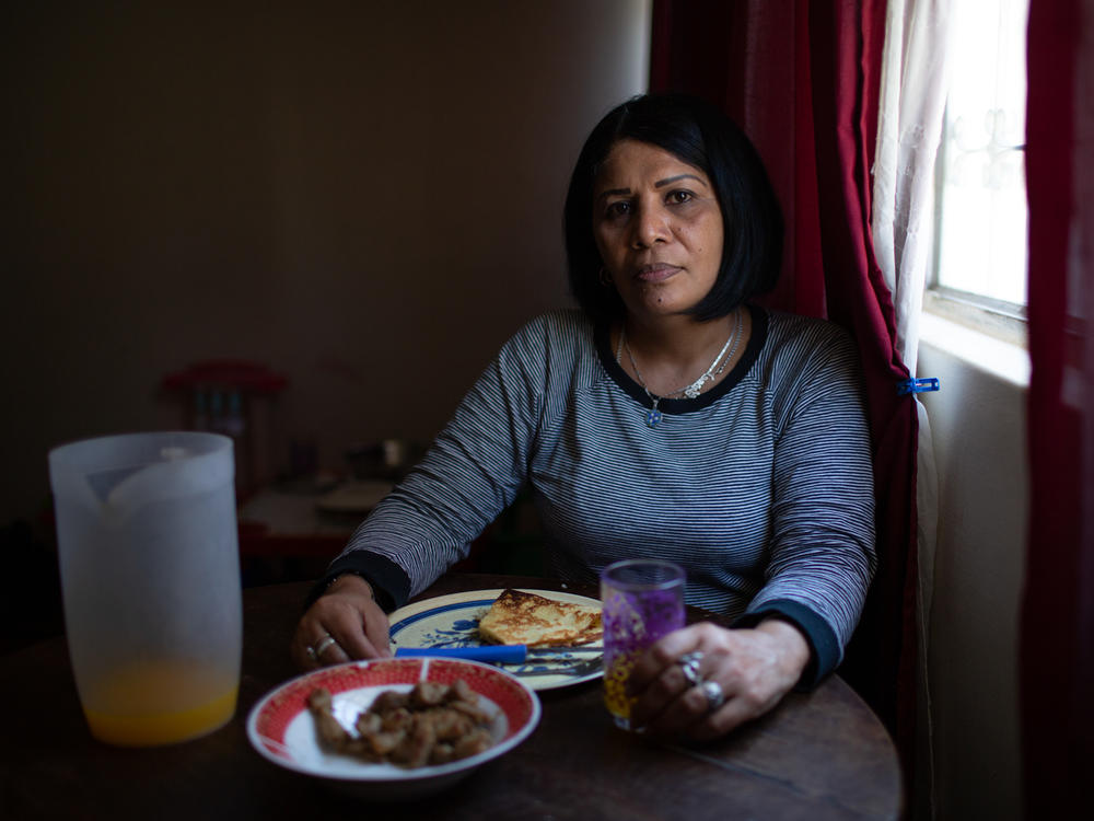 Yroné Camelia Araujo Barreto, a 50-year-old Venezuelan migrant living in Quito, Ecuador, at the dining room table. She is eating a traditional Venezuelan dish of <em>cachapa, </em>round dough made from corn, filled with pork. She typically eats two meals a day if she's lucky enough to afford it.