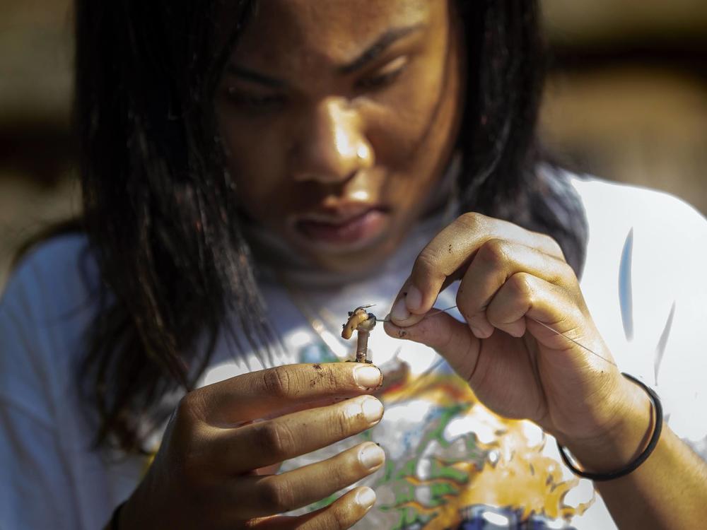 Alaysia Mondon, 14, baits her hook with a worm while fishing on Lake Lashaway.