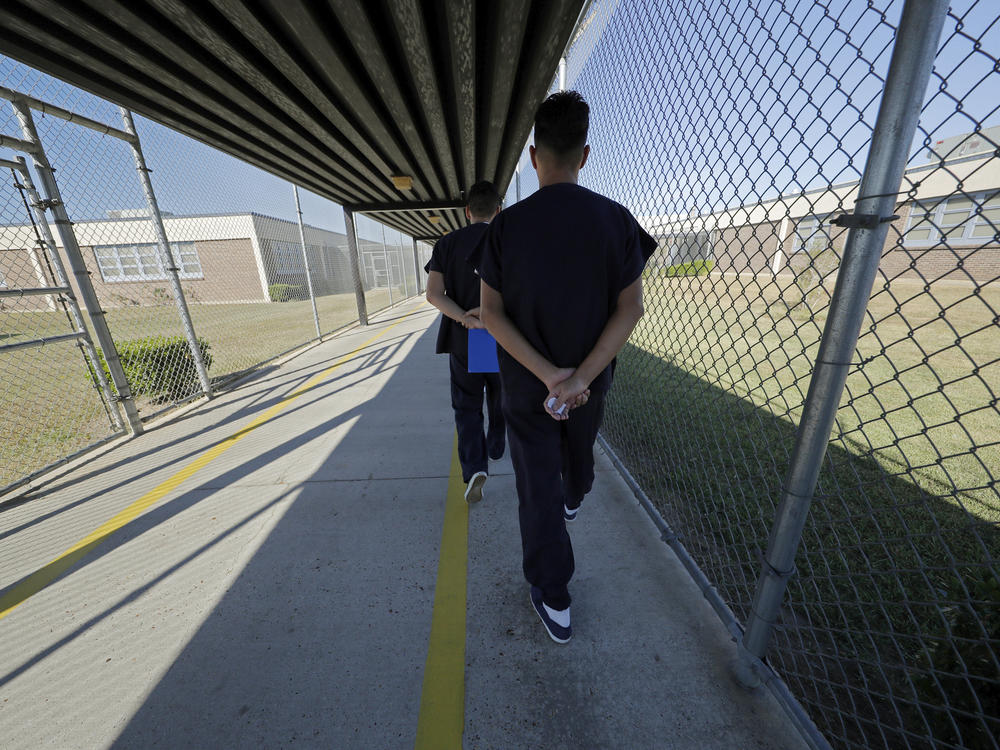 Detainees walk with their hands clasped behind their backs along a line painted on a walkway inside the Winn Correctional Center in Winnfield, La.