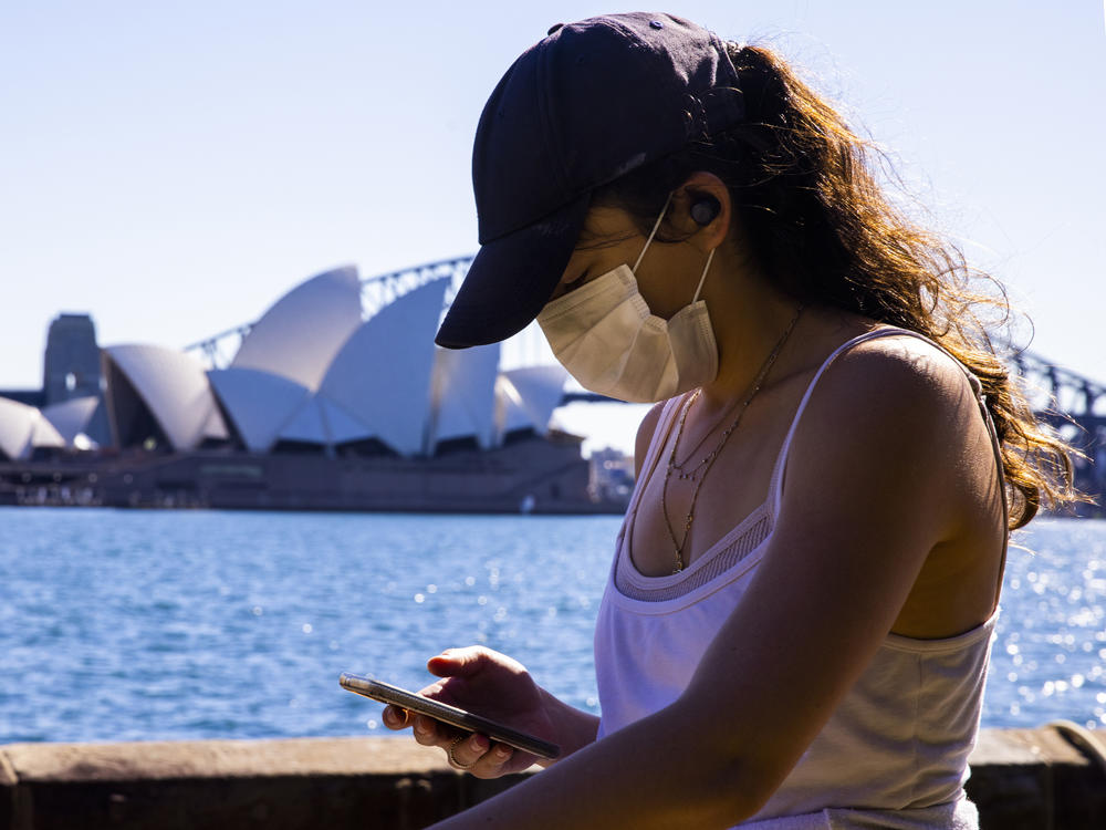 A woman looks at her phone outside the The Royal Botanic Gardens in Sydney, Australia on Aug. 6. The Indicator from Planet Money spoke to an economist for advice on how to cut back on digital dependency.