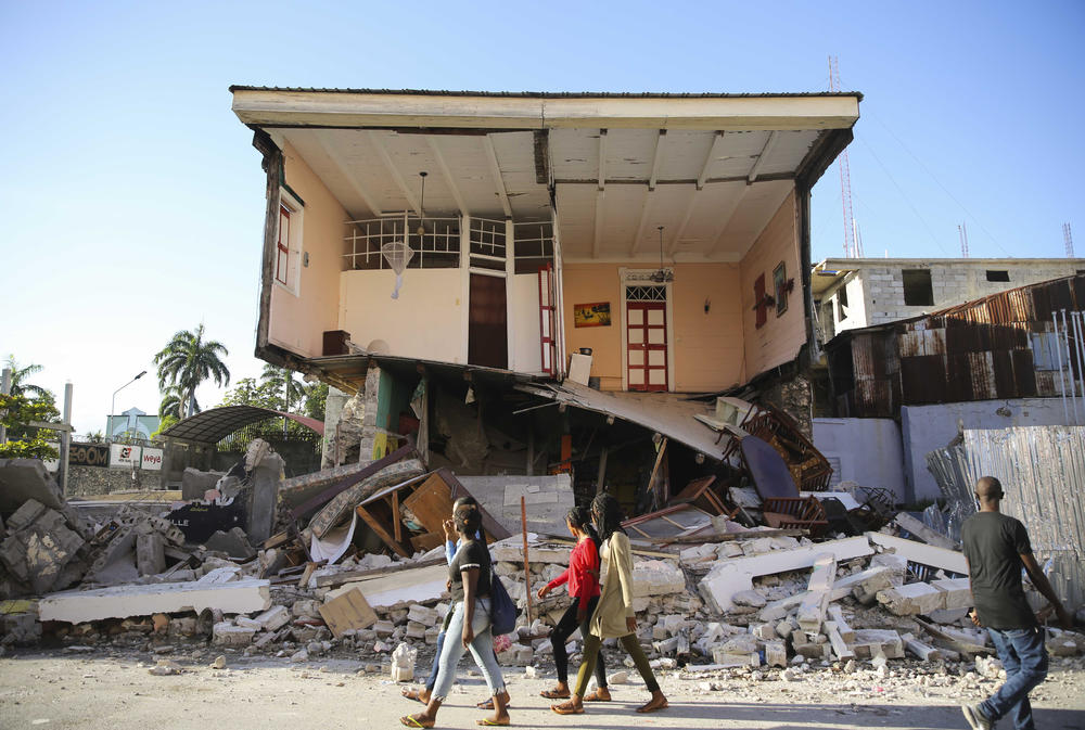 <strong>Sat., Aug. 14:</strong> People walk past a home destroyed by the earthquake in Les Cayes, Haiti.