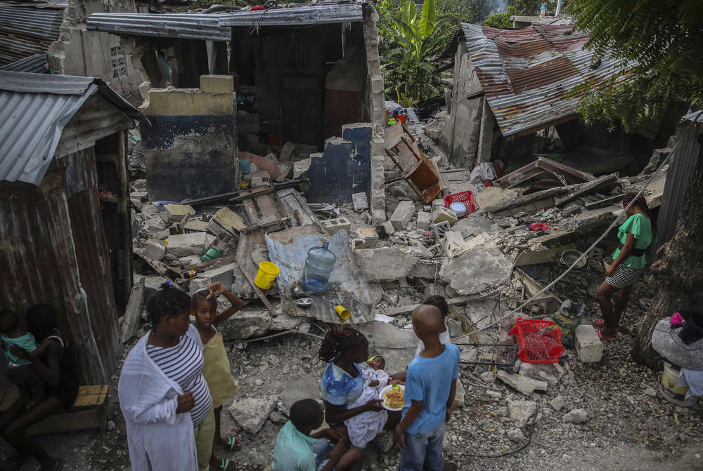 <strong>Sun., Aug. 15:</strong> A family eats breakfast in front of homes destroyed the earthquake in Les Cayes.