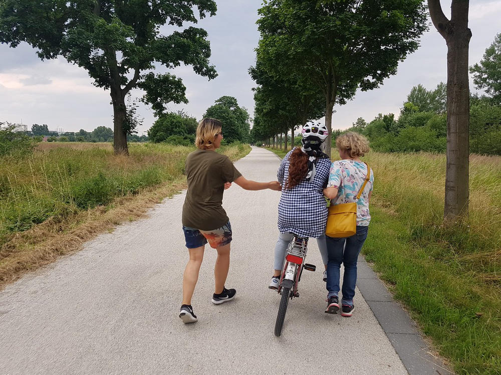 Two women support a refugee as she learns to ride a bike. One woman who participated in the program says, 
