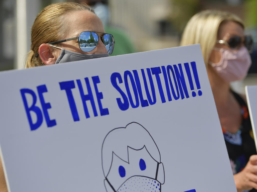 Demonstrators calling on people to wear masks gather outside school district headquarters in Marietta, Ga., last week. A recent review at pandemic data finds requiring masks, capping the size of gatherings and instituting certain bar, gym and restaurant restrictions are all strategies that can help stop a surge in COVID-19 hospitalizations.