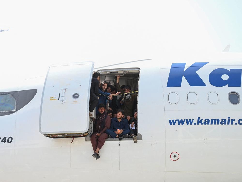 Afghan people climb on a plane and sit by the door as they wait at the Kabul airport.