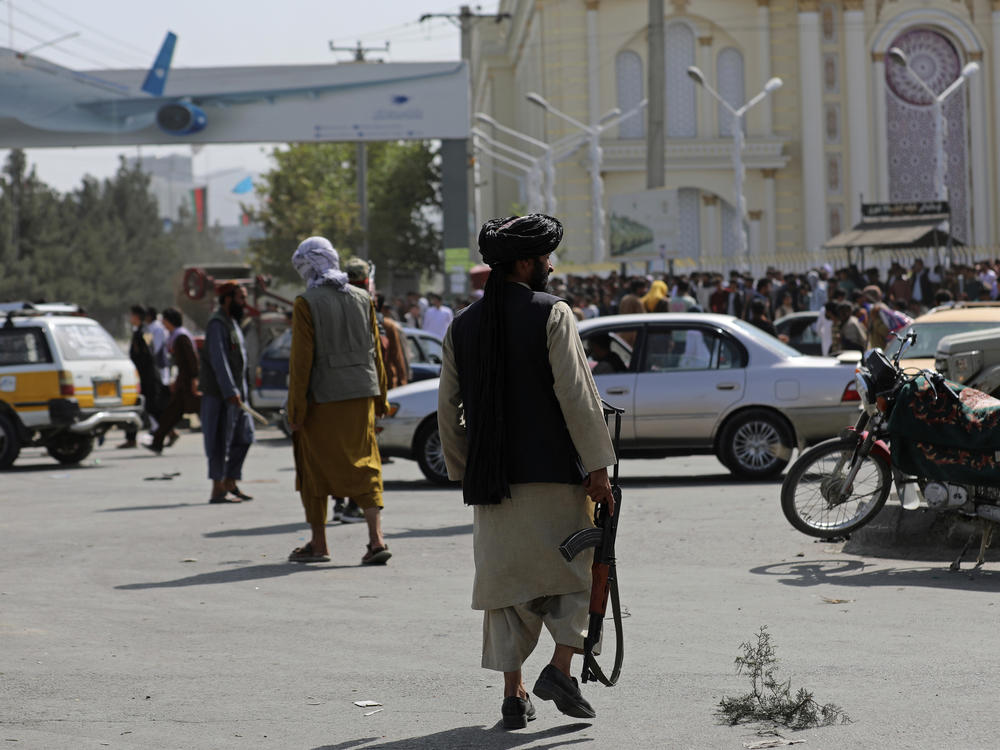 Taliban fighters stand guard in front of the Hamid Karzai International Airport in Kabul, Afghanistan, Monday. Thousands of people packed into the airport, rushing the tarmac and pushing onto planes in desperate attempts to flee the country after the Taliban took over.