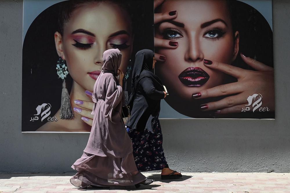 Women on Aug. 7 walk past a billboard put up on the wall of a beauty salon in Kabul.