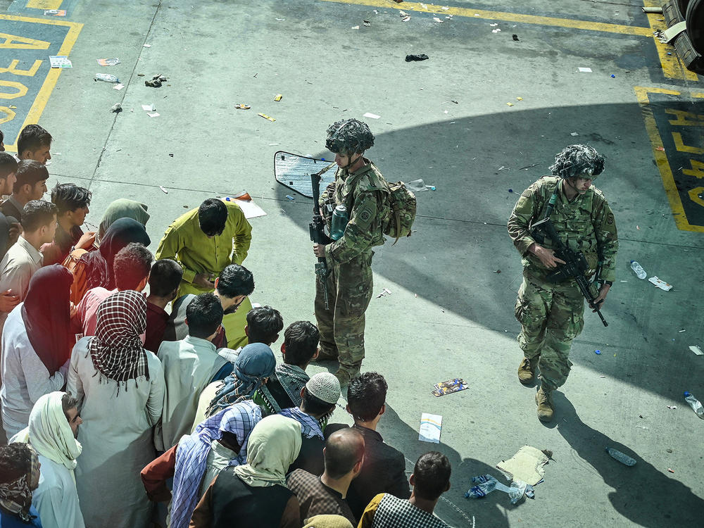 U.S. soldiers stand guard as Afghans wait Monday at the Kabul airport following the swift end to Afghanistan's 20-year war.