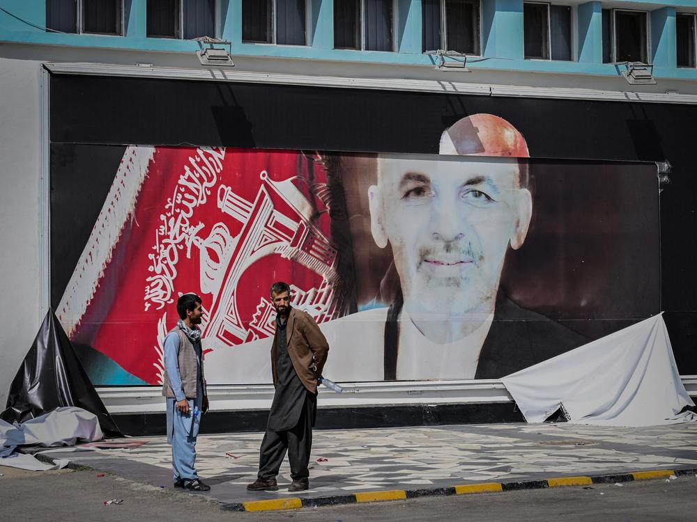 Men stand next to a torn poster of ousted Afghan President Ashraf Ghani at the Kabul airport on Monday. Ghani fled Afghanistan over the weekend as Taliban forces closed in on Kabul.