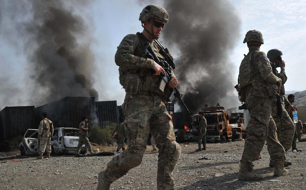 A U.S. soldier walks past burning trucks at the scene of a suicide attack in Afghanistan's Nangarhar province in 2014.