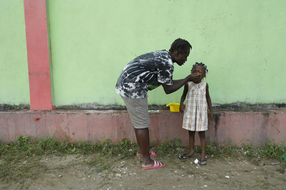 A father cleans his daughter's face at the soccer stadium in Les Cayes on Thursday. The night before, a thunderstorm and an aftershock rattled people staying in the soccer stadium.