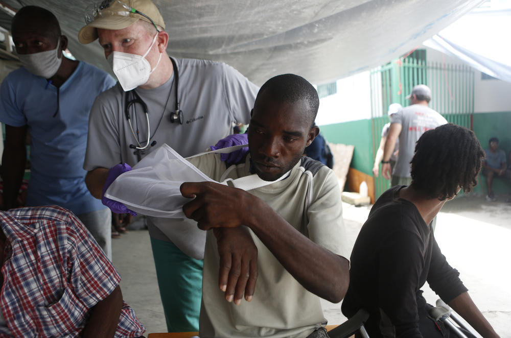 Andrew Patterson with the aid organization Give Hope wraps a sling around John Sanozier for his injured shoulder.