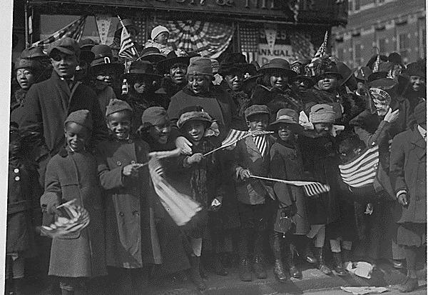 Children and adults line the streets in New York City for a parade welcoming the Harlem Hellfighters after the end of World War I.