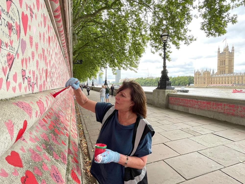 Fran Hall paints hearts on a memorial in London dedicated to people who have died from COVID-19. She and other activists are pushing for the British government to investigate its handling of the pandemic.