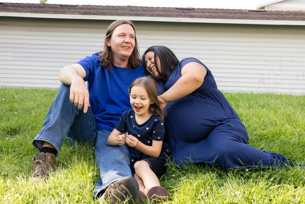 Mat Pergens rests on the grass outside his apartment with his wife, Amanda, and daughter Sylvia. What he really wants is a yard of his own.