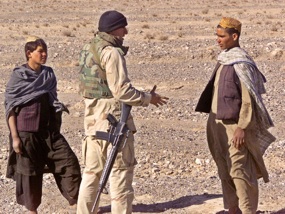Cpl. Ajmal Achekzai, 26, who served as a translator for the 15th Marine Expeditionary Unit, talks with two Afghan locals in December 2001 at the perimeter of a patrol base in southern Afghanistan.