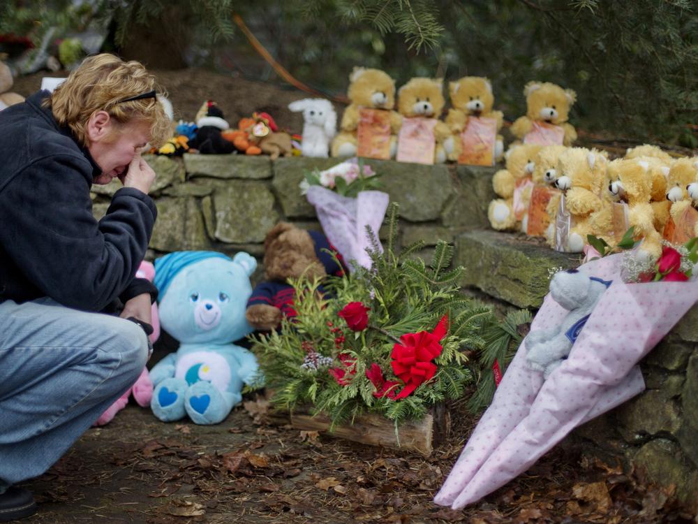 A mourner kneels beside 26 teddy bears, each representing a victim of the Sandy Hook Elementary School shooting, at a sidewalk memorial in 2012 in Newtown, Conn.