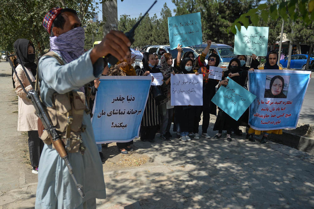 A Taliban fighter stands guard as Afghan women take part in an anti-Pakistan protest in Kabul on Wednesday. At far right, a protester holds a sign with a photo of Banu Negar.