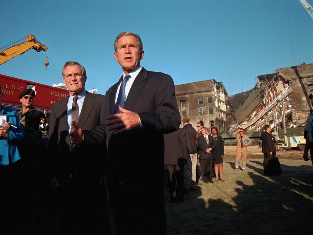President George W Bush gives an address in front of the damaged Pentagon following the Sept. 11 terrorist attack there as Counselor to the President Karen Hughes and Secretary of Defense Donald Rumsfeld stand by.