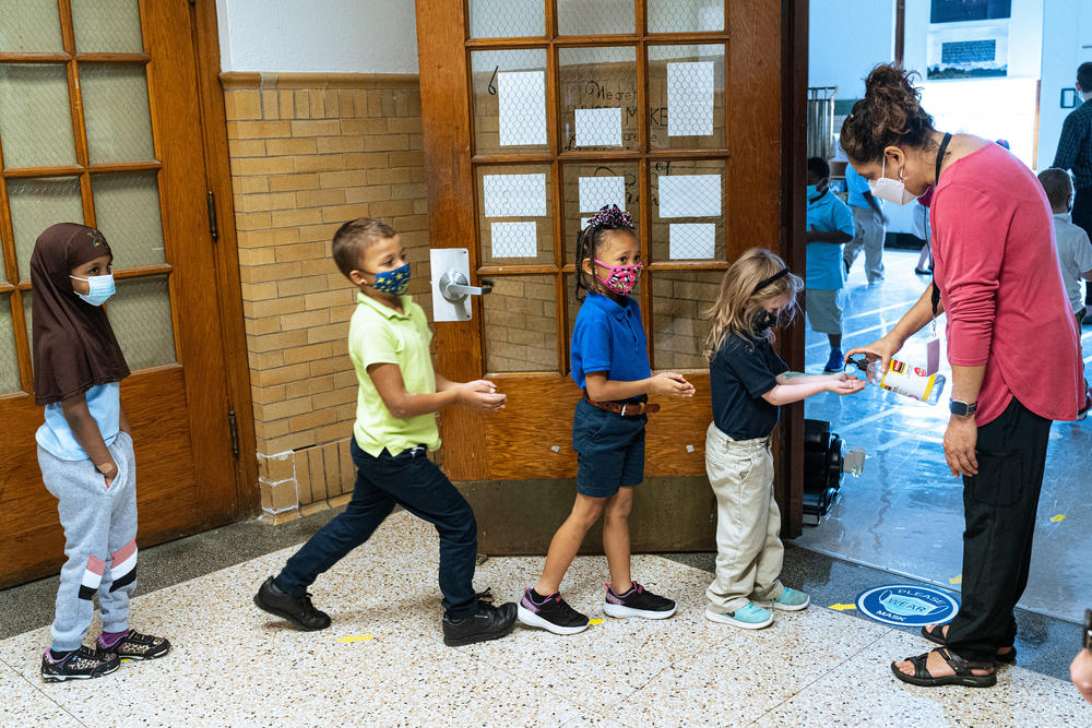 Quesada greets her second grade music class and gives them each a squirt of hand sanitizer as they enter her classroom.
