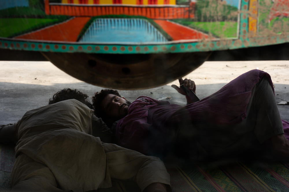 With border traffic at a standstill, men rest under a truck while waiting to get into Afghanistan.