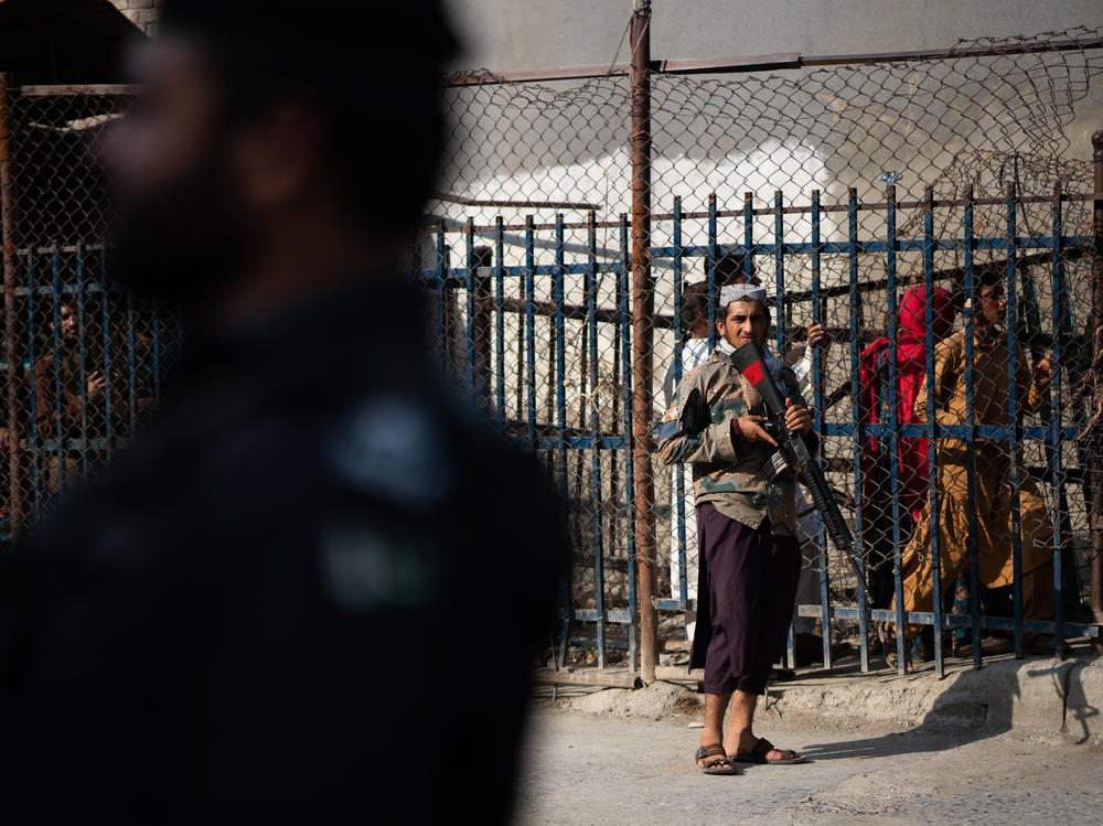A Taliban guard stands on the Afghan side of the Torkham border crossing with Pakistan. People behind wait either to leave Afghanistan or to receive those returning to the country.