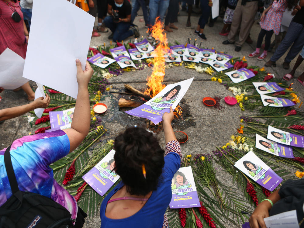 People place small posters depicting Honduran environmental activist Berta Caceres next to a fire as they wait outside the Palace of Justice for the verdict in the activist's murder case. A little over five years after Caceres' murder, an ex-chief of the energy company Desa has been found partly guilty.
