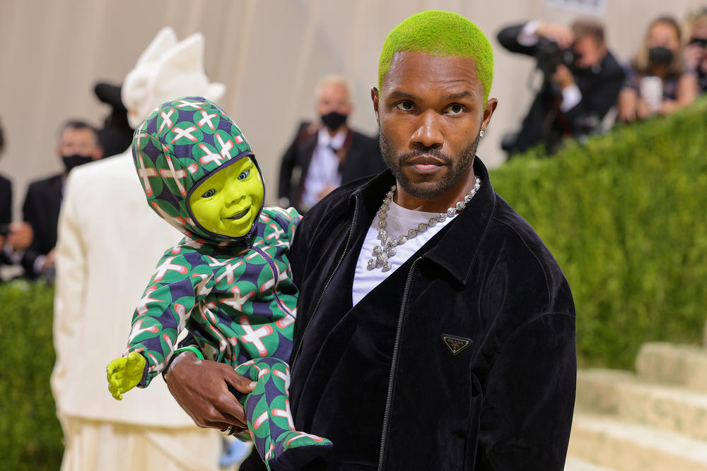 Frank Ocean, wearing a Prada suit jacket, carries a ... green robot-puppet-doll? A <a href=