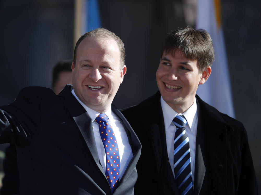 Colorado Gov. Jared Polis, left, waves to the crowd accompanied by his partner, Marlon Reis, in 2019. The two were married Wednesday, marking the first same-sex marriage of a sitting governor.