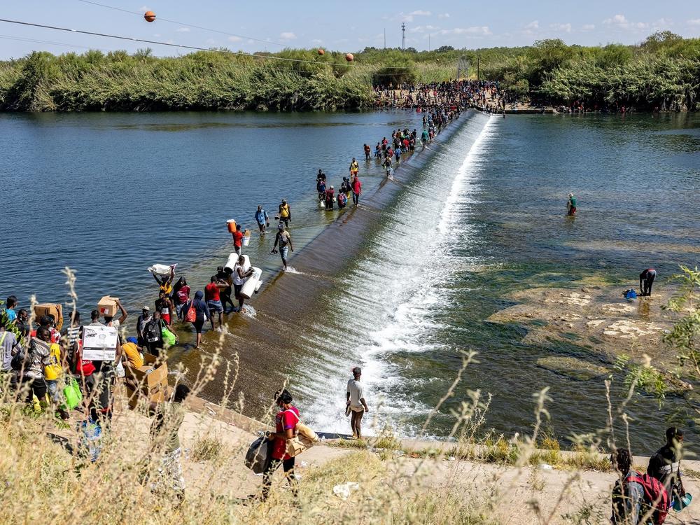 Migrants walk across the Rio Grande River carrying food and other supplies back to a makeshift encampment under the International Bridge in Del Rio, Texas, on Friday.