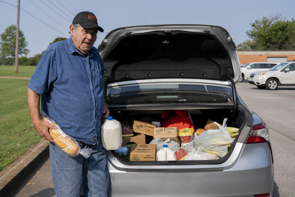 Abshier stands outside his car after receiving groceries from the food bank. The items include milk, yogurt, cherry tomatoes, bread, eggs, bok choy, cabbages, grapes and mini cherry pies.