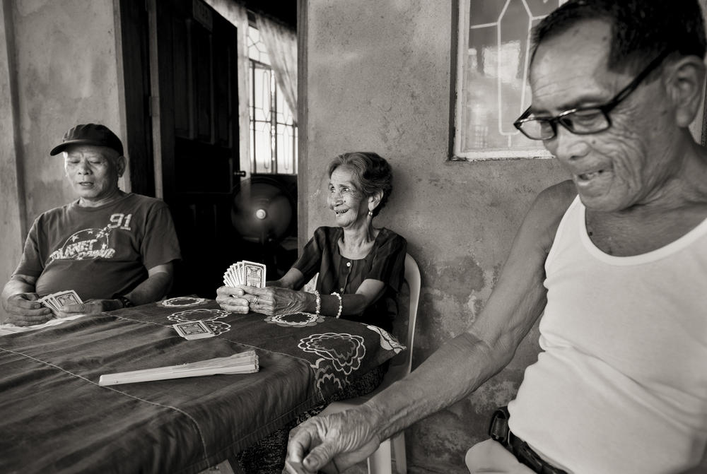 Emilia dela Cruz Mangilit, 92, center, plays a game of cards with her neighbors Abelardo Hernandez and Cezar Lalu, left and right. Mangilit was 15 years old when her village of Mapaniqui in Pampanga was shelled and then raided by the Japanese during World War II.