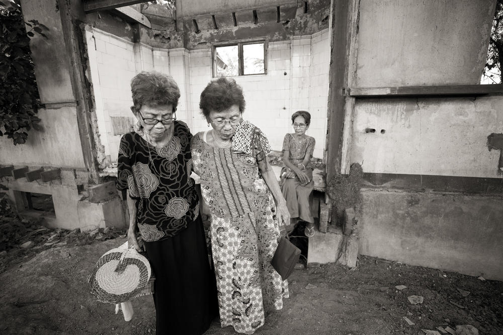 Belen Alarcon Culala and Pilar Quilantang Galang, left and right, support each other during a visit to the Red House, where the women were raped repeatedly as children by the Japanese Imperial Army soldiers. In the background is Emilia Mangilit, a fellow survivor. Culala died on Feb. 28, 2021.