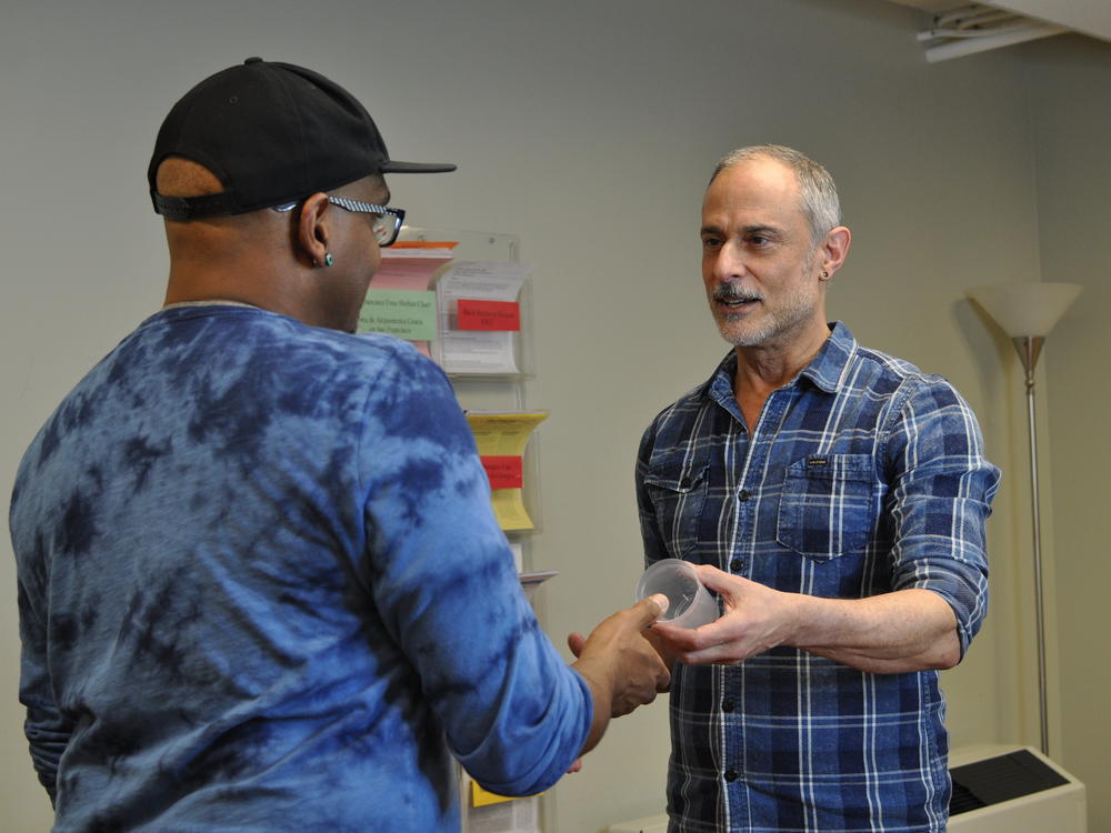 At the San Francisco AIDS Foundation, staff members Tyrone Clifford (left) and Rick Andrews (right) demonstrate how a contingency management visit typically begins, with a participant picking up a specimen cup for a urine sample. If the sample tests negative for meth or cocaine use, the participant has an incentive dollar amount added to their 