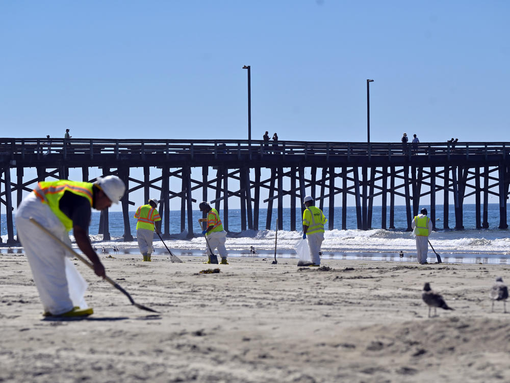 Workers clean oil from the sand, south of the pier, in Newport Beach, Calif., Tuesday, Oct. 5, 2021. A leak in an oil pipeline caused a spill off the coast of Southern California, sending about 126,000 gallons of oil into the ocean, some ending up on beaches in Orange County.