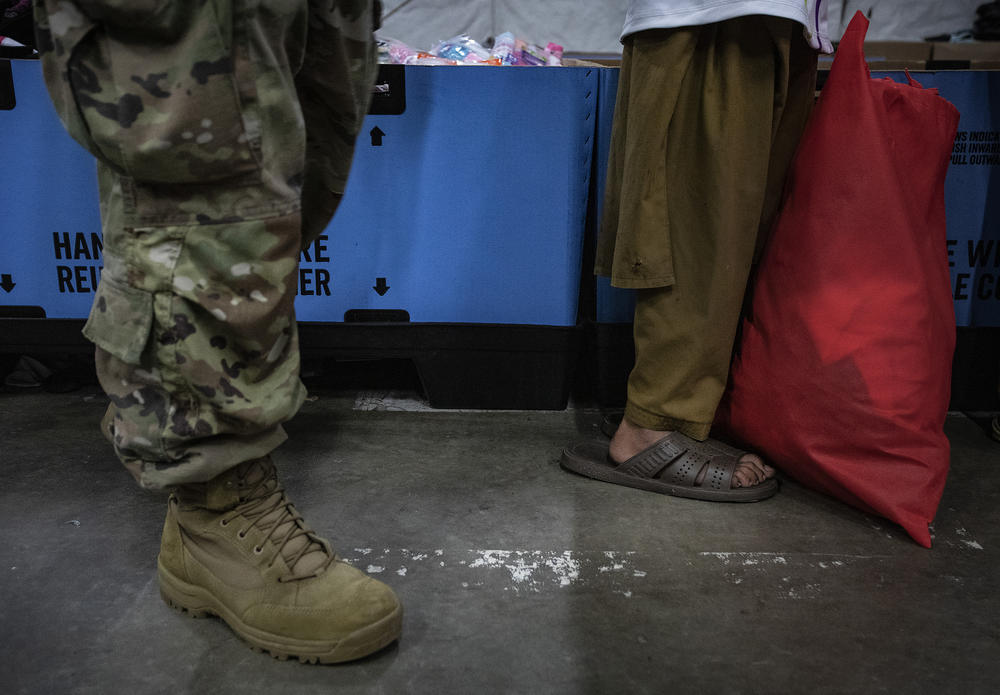 Standing in front of a soldier, a young Afghan refugee, who is partially blind, waits in line for new clothes at the military base.