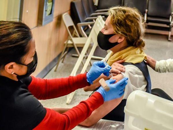 Margaret Applegate (in yellow scarf), a United Airlines customer service agent, is accompanied by Lori Augustine, vice president of United's San Francisco hub, as Applegate gets a COVID-19 vaccine in September ahead of United's mandated deadline.