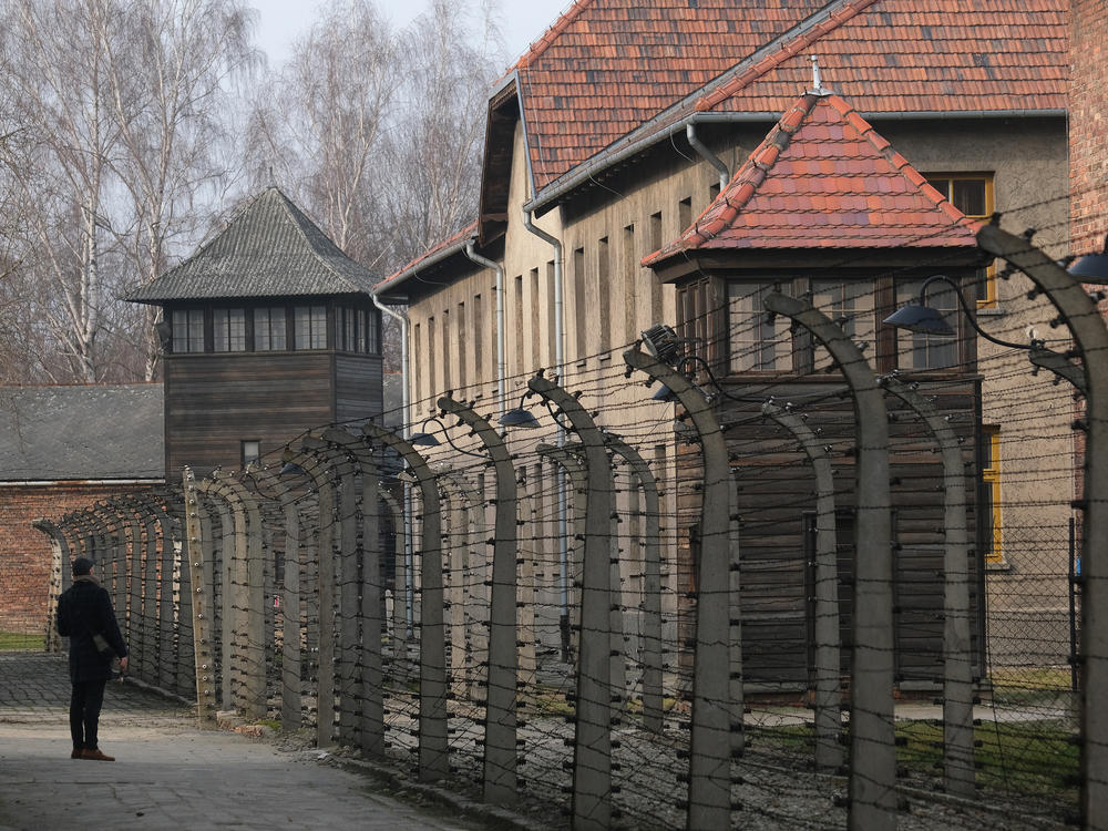 A visitor walks near barbed wire and prison barracks at the former Auschwitz I concentration camp on Jan. 26, 2020, in Oswiecim, Poland.
