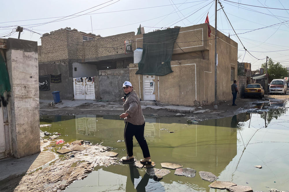 Electoral candidate Taghrid Mohammed Alkhazali crosses a street filled with sewage mixed with wastewater in a Baghdad slum. She is from a new political party that is running on a platform promoting better public services for Iraqis.
