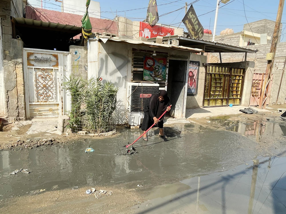 Najiha Daher sweeps sewage and wastewater away from the door of her grocery store in a slum district of Baghdad. Corruption and dysfunction in government have left Iraqis with crumbling public services, in a country that is rich with oil.