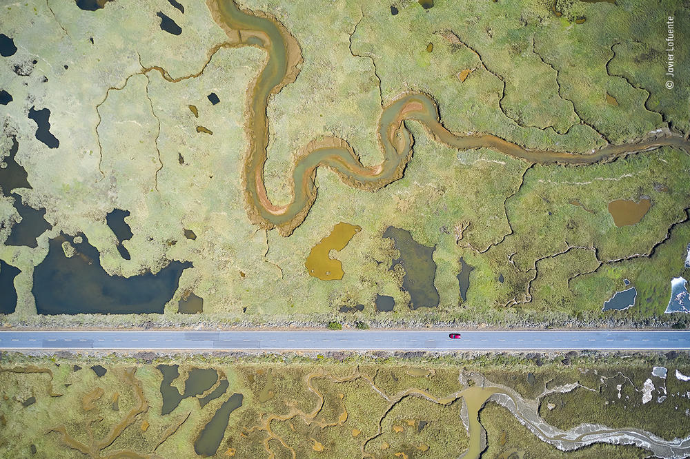 <em>Road to ruin</em>, by Javier Lafuente, Spain, winner, category: Wetlands - The Bigger Picture. Lafuente shows the stark, straight line of a road slicing through the curves of a wetland landscape. By maneuvering his drone and inclining the camera, Lafuente dealt with the challenges of sunlight reflected by the water and ever-changing light conditions.